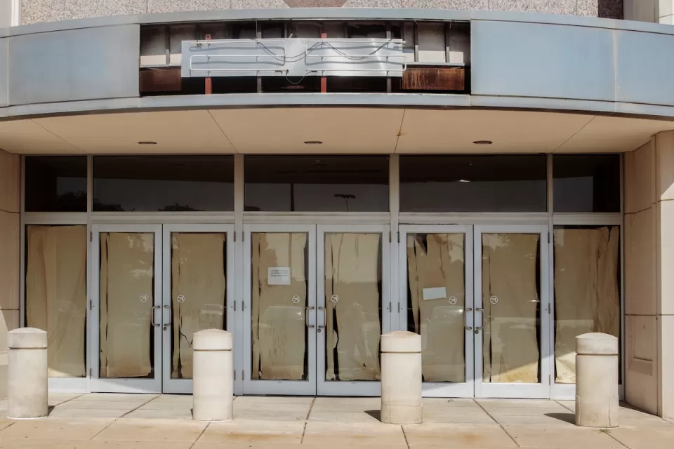 Vacant retail storefront with multiple glass doors lined with brown paper and a removed neon sign.